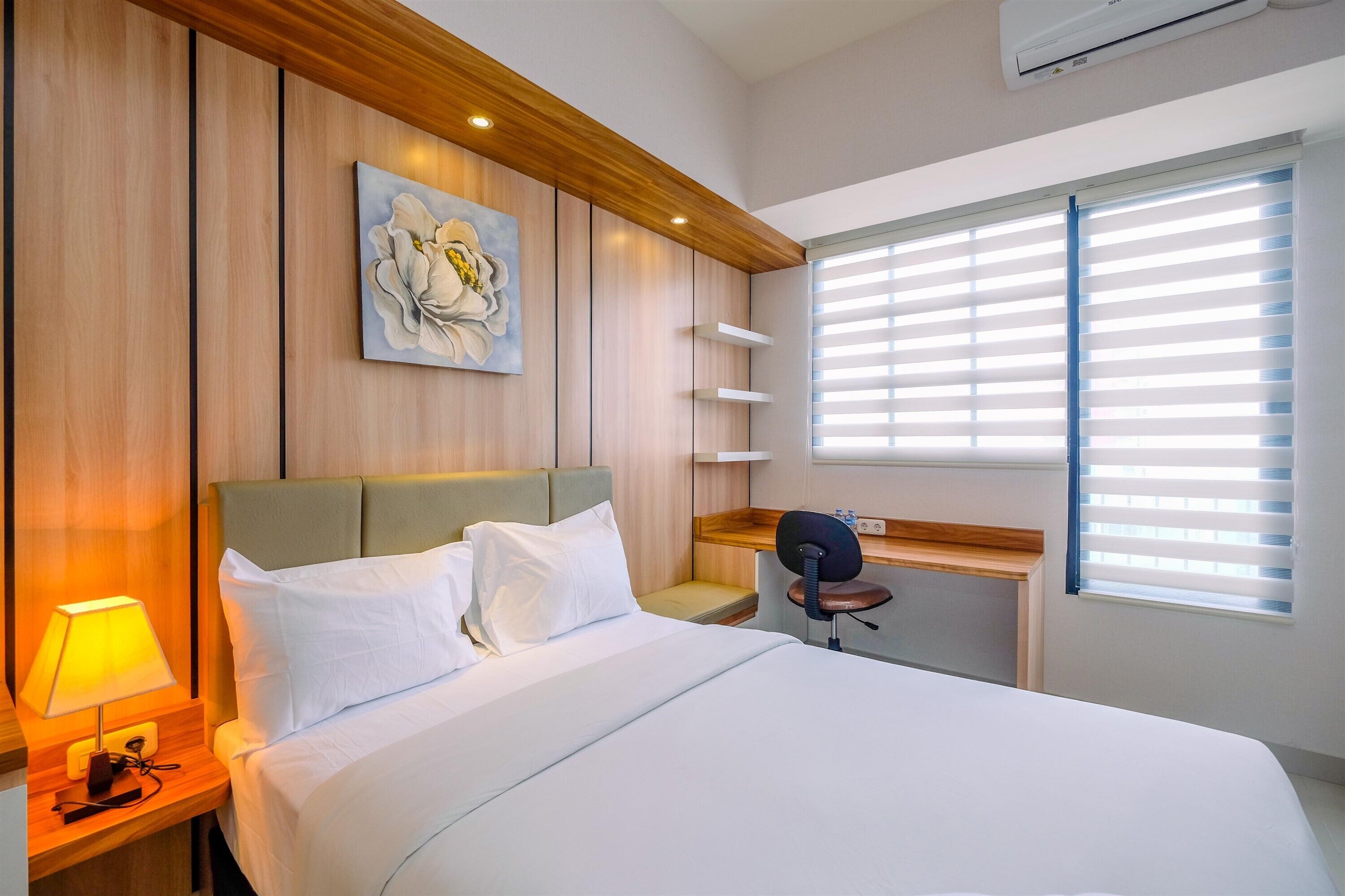 A modern hotel room with a large bed, a desk, a chair, and a wall-mounted air conditioner.