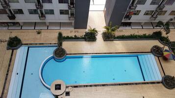 A rooftop swimming pool surrounded by greenery and modern buildings.