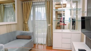 A modern living room with a light blue sofa, a glass coffee table, a flat-screen TV, and a glass cabinet with shelves. - Nice And Homey 1Br At The Wave Kuningan Apartment (Jakarta)