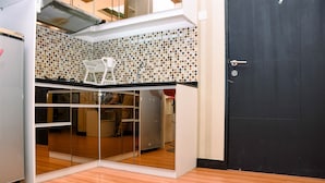 A compact kitchen with a tiled backsplash, a white chair, and a sliding door leading to a living area. - Nice And Homey 1Br At The Wave Kuningan Apartment (Jakarta)