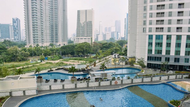 A large outdoor swimming pool area with multiple pools, surrounded by greenery and modern buildings. - Nice And Homey 1Br At The Wave Kuningan Apartment (Jakarta)