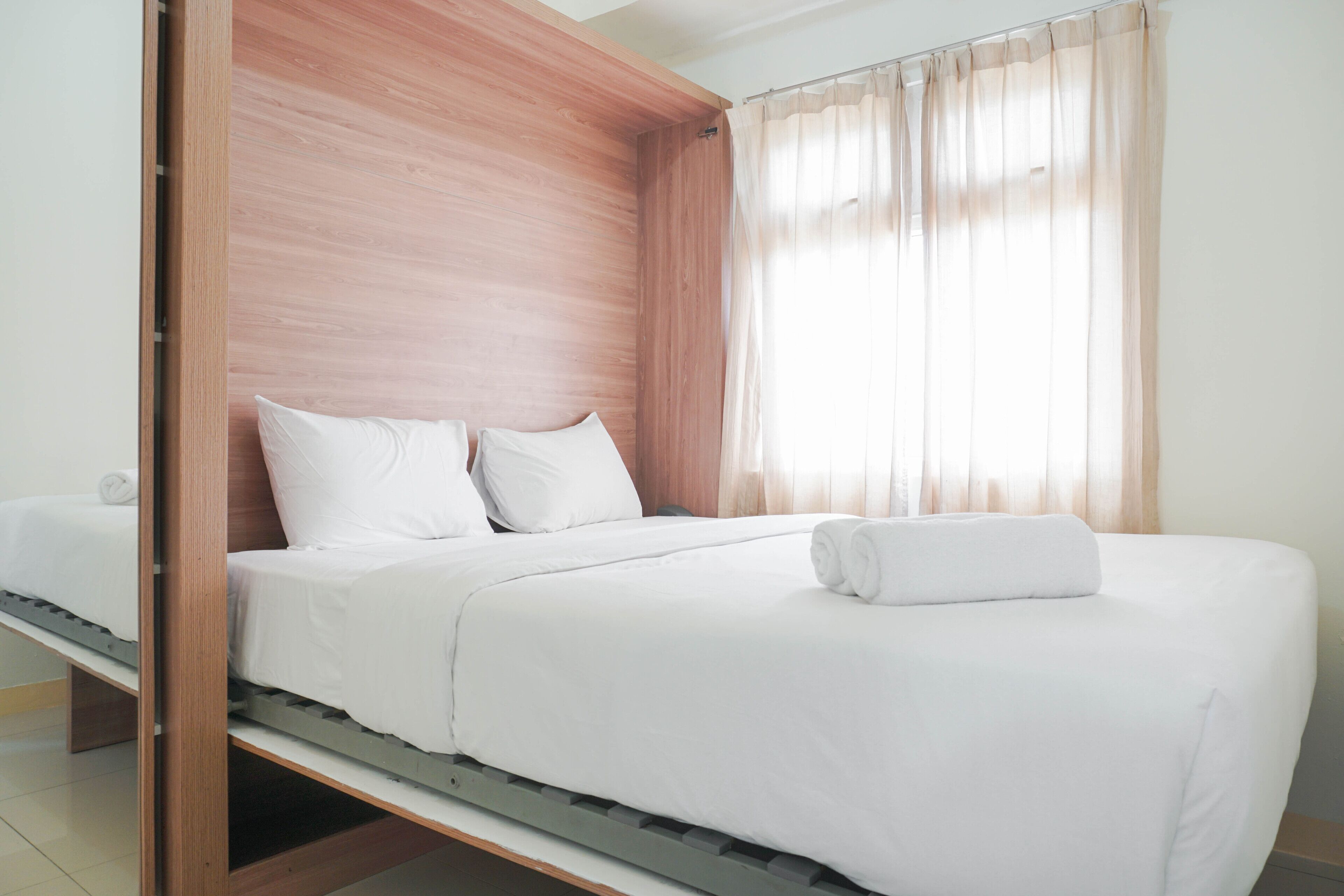 A single bed with white bedding, a wooden headboard, and a window with sheer curtains.