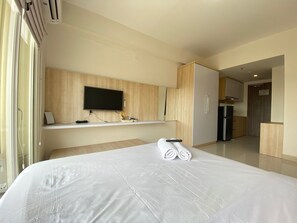 Une chambre d’hôtel dotée d’un grand lit, d’un téléviseur à écran plat fixé au mur, d’un minibar et d’un coin cuisine séparé.