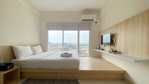 Habitación de hotel moderna con una cama grande, un televisor montado en una pared de madera y vistas de la ciudad a través de amplias ventanas.