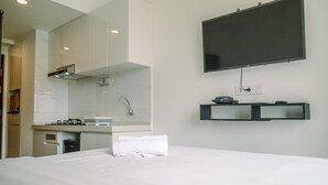 A hotel room with a bed, a TV mounted on the wall, a small kitchen area, and a mirror. - Comfortable Studio With Pool View At Sky House Bsd Apartment (Pagedangan)