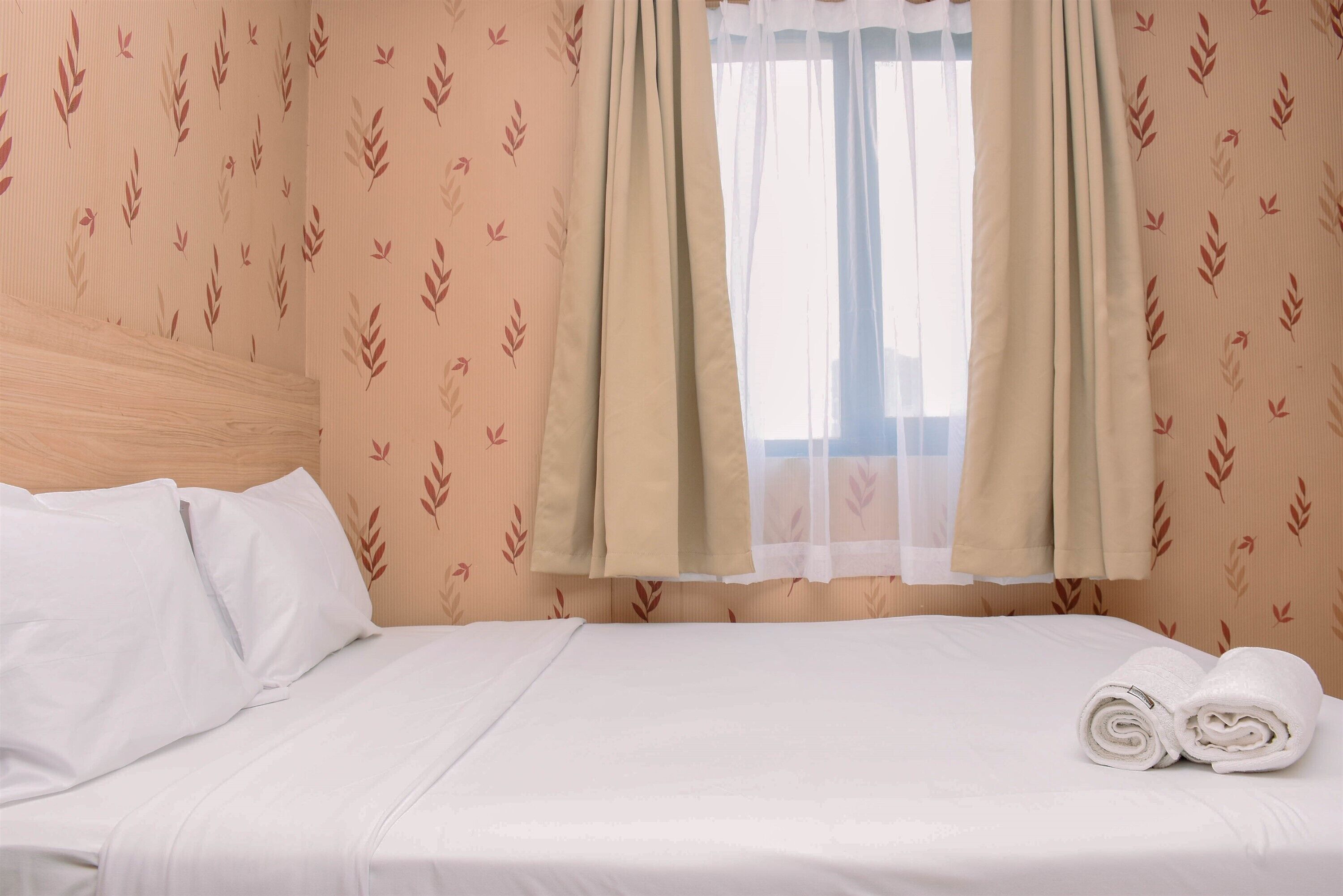A neatly made bed with white linens, beige curtains, and a window with a view.