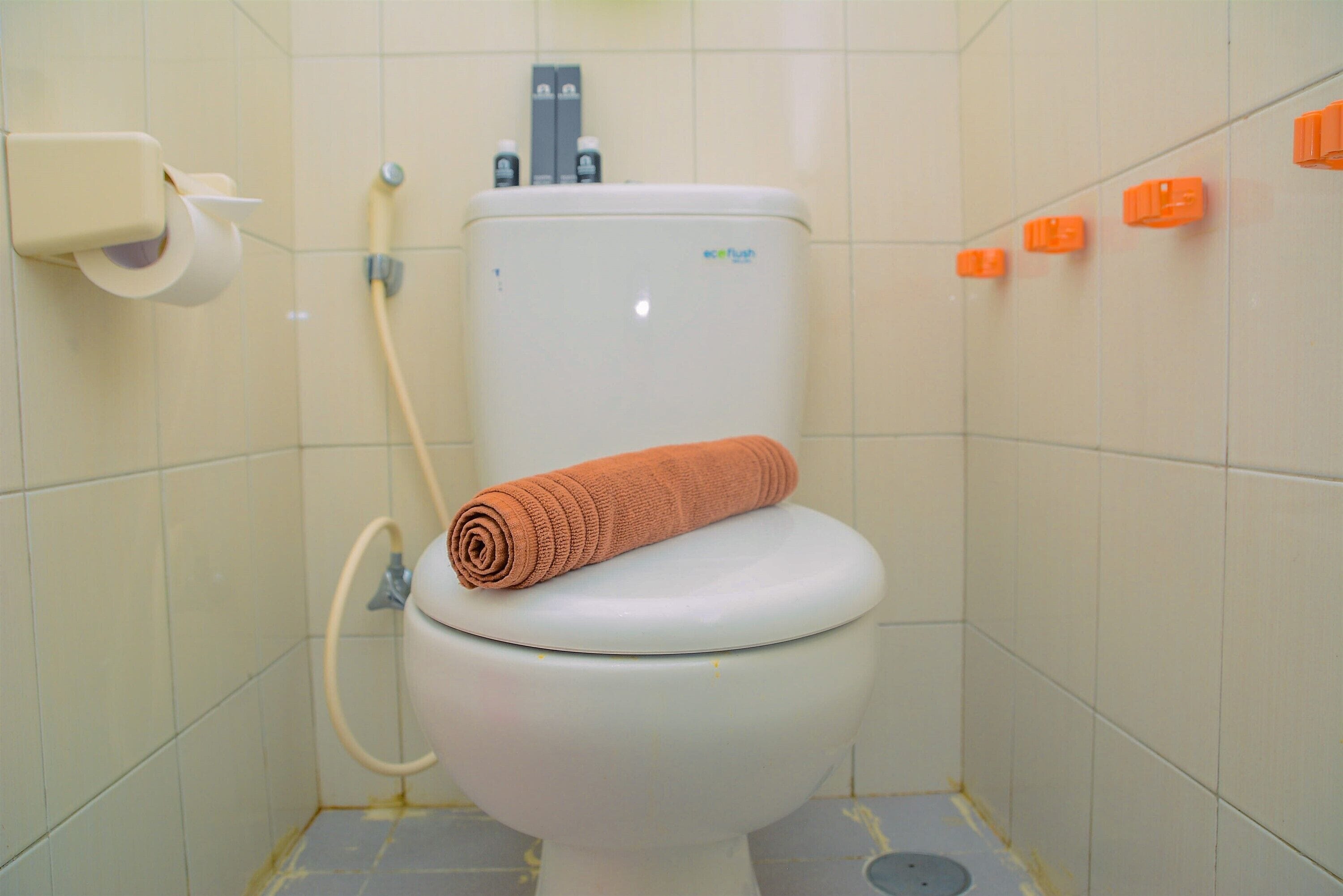 Inodoro con un rollo de papel higiénico, tanque de agua y secamanos.