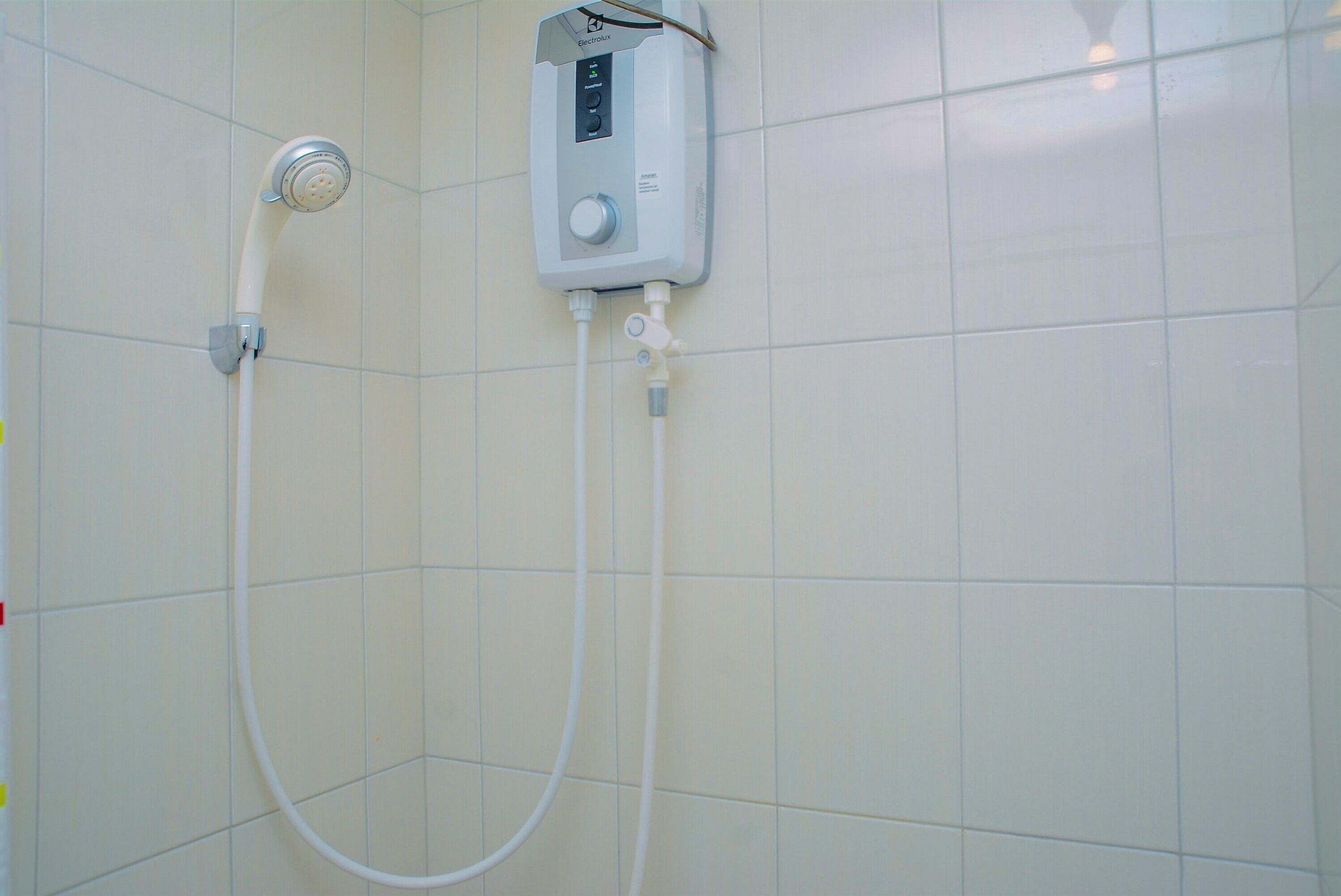 A shower with a control panel and a handheld showerhead mounted on a tiled wall.