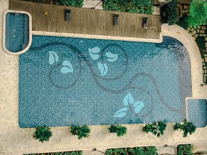 Vista aérea de una piscina con diseño de mosaico, rodeada de palmeras y una terraza de madera.