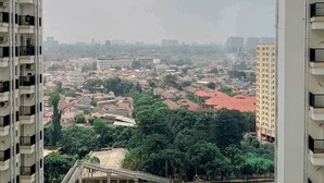 A high-rise building with multiple balconies, a view of a cityscape with various buildings and greenery, and a bridge in the foreground.