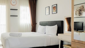 Ein modernes Hotelzimmer mit einem großen Bett, einem Schreibtisch mit Fernseher, einem Kleiderschrank und einer Wanduhr.
