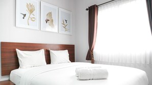 A neatly made bed with white linens and a folded towel, a wooden headboard, and three framed botanical prints on the wall. - Modern 2Br At Signature Park Grande Apartment (Jakarta)