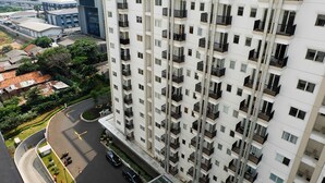 A high-rise building with multiple balconies, a parking area, and surrounding greenery.