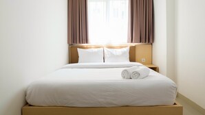 A neatly made bed with white linens, a wooden headboard, and a window with brown curtains.