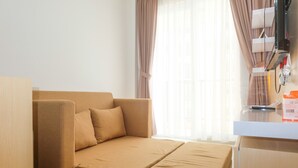 A modern hotel room with a sofa bed, a desk with a computer, and a window with sheer curtains.