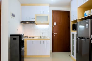 A compact kitchen with white cabinets, a built-in microwave, a refrigerator, and a gas stove.