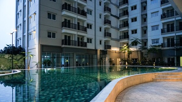 A modern hotel with a large indoor swimming pool, multiple balconies, and a well-lit entrance area.