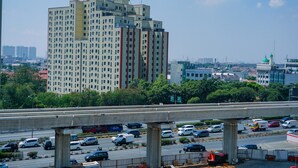 Un edificio de varios pisos con diseño moderno, rodeado de vegetación y una autopista concurrida.