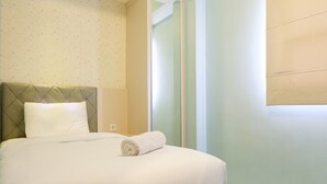 A neatly made bed with a rolled white towel, a quilted headboard, and a plain wall with a subtle pattern.