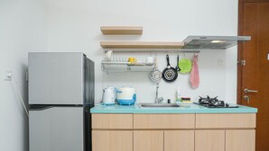 A compact kitchen with a refrigerator, a sink, and a stove. There are hanging pots and pans, a dish rack, and a microwave on the countertop. - Modern 1Br Apartment At Signature Park Grande (Jakarta)