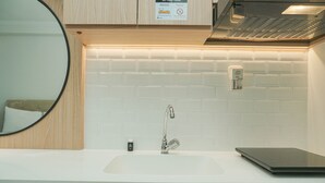 Une salle de bain moderne avec un lavabo blanc, un miroir et un ordinateur portable posé sur le comptoir.