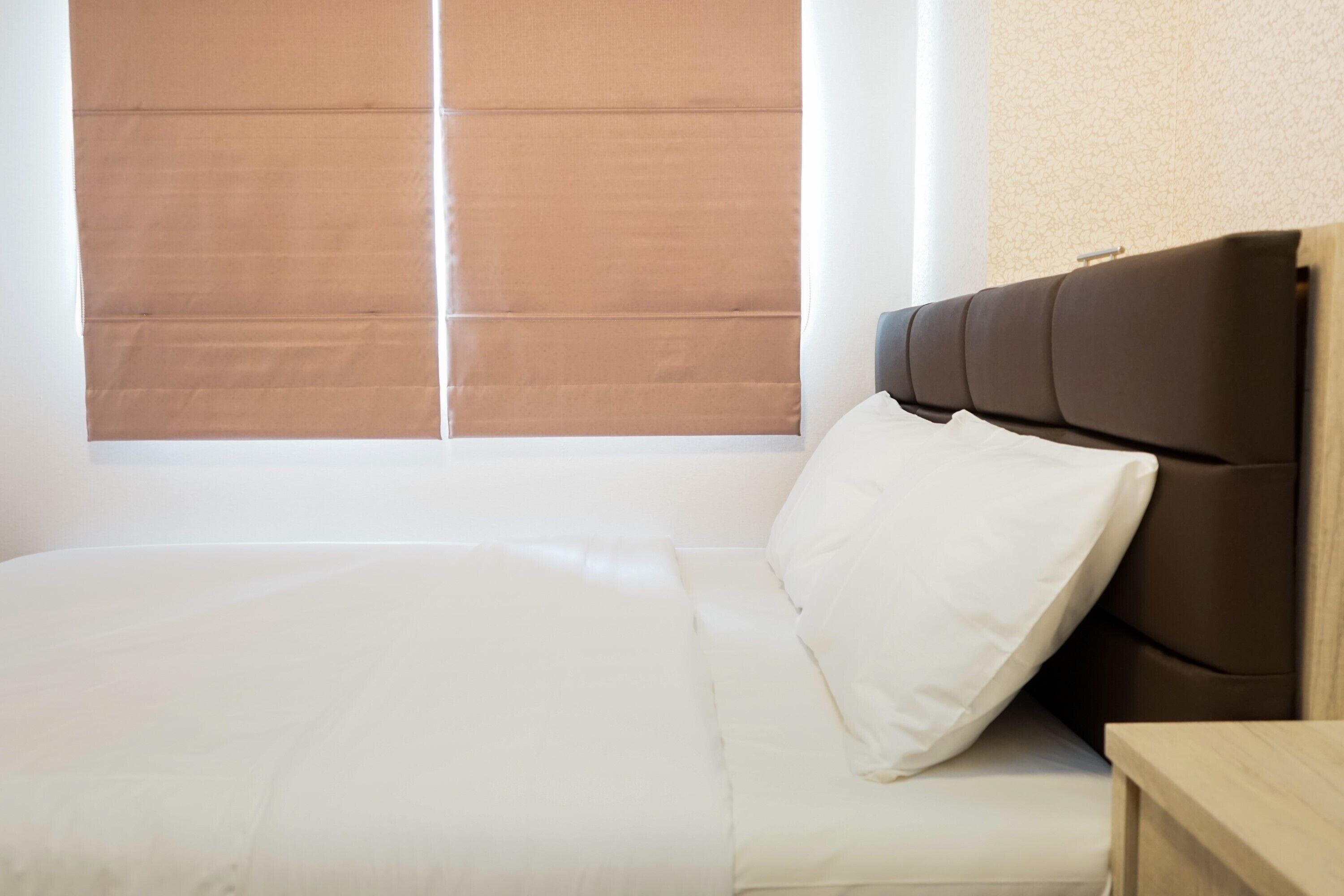 A neatly made bed with white linens in a room with a large window and a wooden headboard.