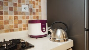 Una cocina con estufa a gas, una olla arrocera Philips morada y blanca, y un hervidor plateado sobre una encimera blanca.