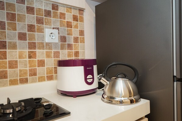 A kitchen with a gas stove, a purple and white Philips rice cooker, and a silver kettle on a white countertop.