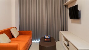 Una sala de estar moderna con una cortina gris, un sofá naranja, una mesita de centro con una bandeja y un televisor montado en la pared.