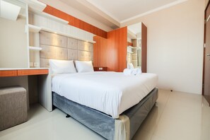 A modern hotel room with a large bed, a bedside table, a built-in wardrobe, and a small seating area. - Great Location 1Br Signature Park Grande Apartment (Jakarta)