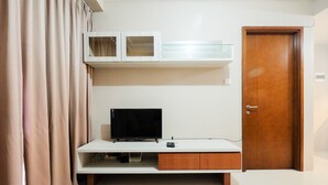 A room with a television on a white stand, a wooden door, and a white cabinet above the stand. - Great Location 1Br Signature Park Grande Apartment (Jakarta)