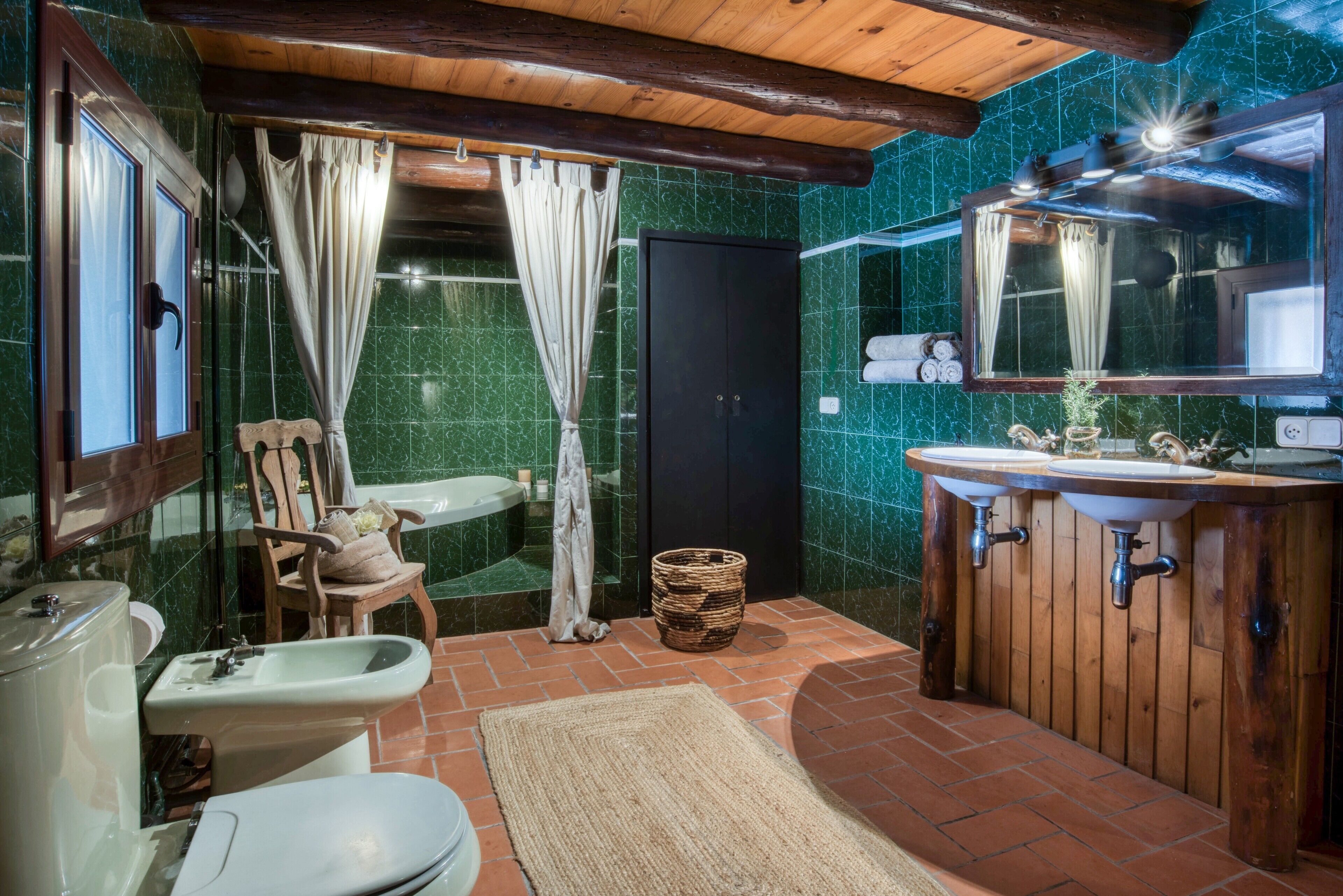 A bathroom with a wooden vanity, a toilet, a bidet, a shower with curtains, and a mirror.