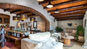 A rustic interior with exposed brick walls, wooden beams, a wooden bench, a sofa, and a round wooden table.
