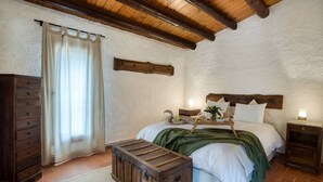 A bedroom with a wooden headboard, a dresser, a bedside table with a lamp, and a window with curtains.