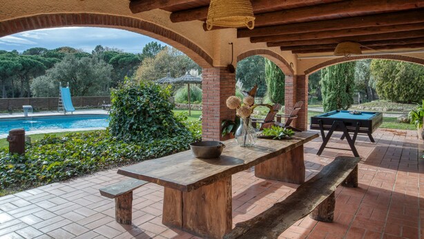 An outdoor patio with a pool table, wooden benches, and a brick wall.