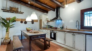 A rustic kitchen with wooden beams, a hanging light fixture, a wooden bench, and a tiled backsplash.