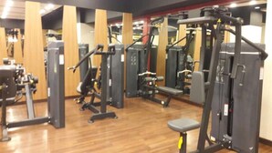 Een sportschool met diverse fitnessapparaten, houten vloeren en spiegels aan de muur.
