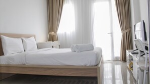 Een hotelkamer met een houten bed, witte beddengoed, een bureau met een computer en gordijnen.