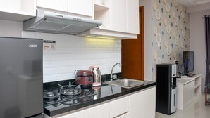 Una cocina moderna con armarios blancos, un refrigerador de acero inoxidable, una estufa a gas, una cafetera y un dispensador de agua.