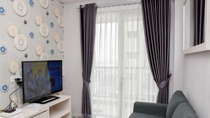 Una sala de estar con una televisión de pantalla plana, una mesa de centro de vidrio, un sofá gris y cortinas estampadas.