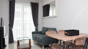 Una sala de estar moderna con un sofá gris, una mesa de centro de vidrio y sillas de madera. Una caja negra con la etiqueta 'Travelio' está sobre la mesa.
