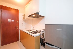 A compact kitchen with a wooden door, a stainless steel refrigerator, a built-in oven, and a sink.