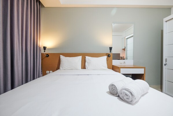 A hotel room with a neatly made bed, a wooden headboard, a bedside table with a lamp, a mirror, and a wardrobe.