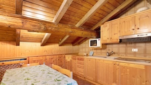 Un interior de madera con una mesa de comedor, sillas, una zona de cocina con armarios, microondas y fregadero.