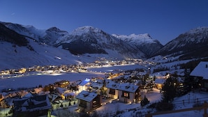 Un pueblo cubierto de nieve al atardecer, con edificios iluminados y vistas de las montañas circundantes.