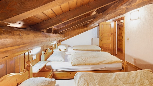 Un dormitorio estilo ático con tres camas, vigas de madera y un aparador de madera.