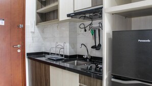 Una cocina con encimera negra, armarios blancos, un refrigerador Panasonic y una puerta de madera.