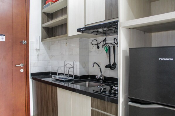 Una cocina con encimera negra, armarios blancos, un refrigerador Panasonic y una puerta de madera.