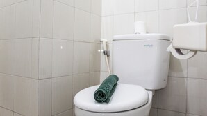 Un inodoro blanco con una toalla verde sobre el asiento y un dispensador de papel higiénico en la pared.