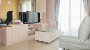 A modern living room with a flat-screen TV, a glass-top coffee table, a sofa, and a TV stand with a flat-screen TV. - Comfy 2Bedroom At Signature Park Grande Apartment (Jakarta)